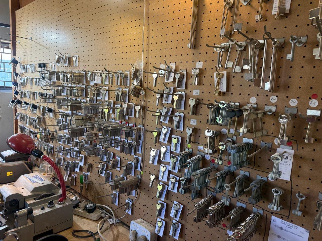 Pegboard of house, gate and padlock key blanks beside the key cutting machine
